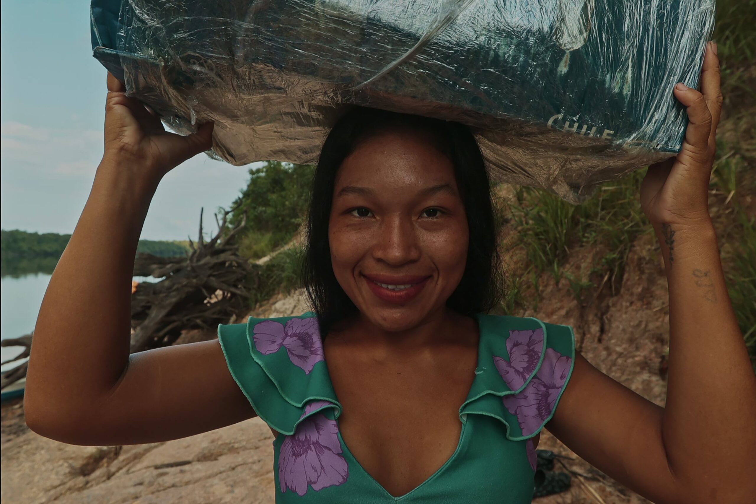 An indigenous woman balancing a package on her head, laughing.